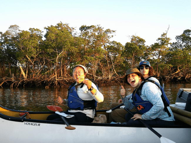 three young people smile from a canoe