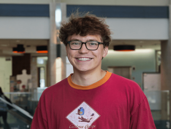 a young white man with brown hair wearing glasses and a red t-shirt