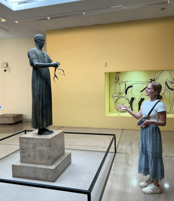 Maggie Matuszak (’27) poses with her presentation subject, The Charioteer, Archaeological Museum of Delphi