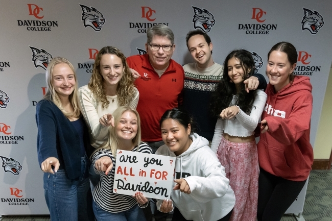 President Doug Hicks poses with a group of students with a handwritten sign: "Are You All In for Davidson?"