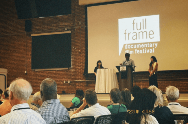 a stage with people talking on it and a screen that reads "Full Frame Documentary Film festival"