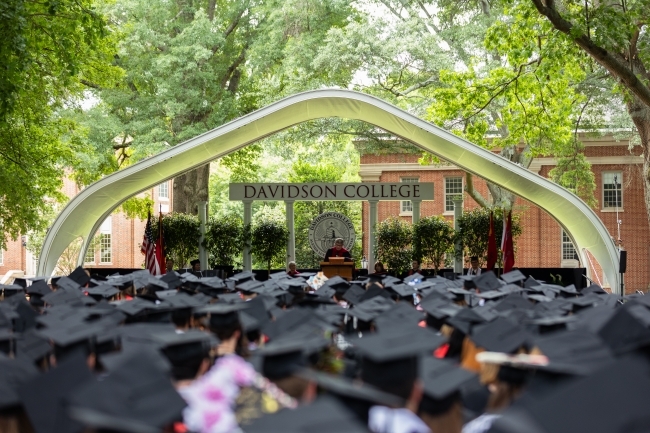 a graduation ceremony on a sunny day under a bunch of big trees