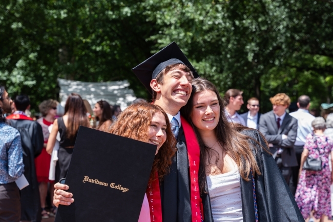 three young people smile together while wearing graduation regalia