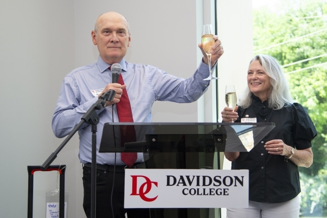 an older white man and woman toast champagne glasses at a podium