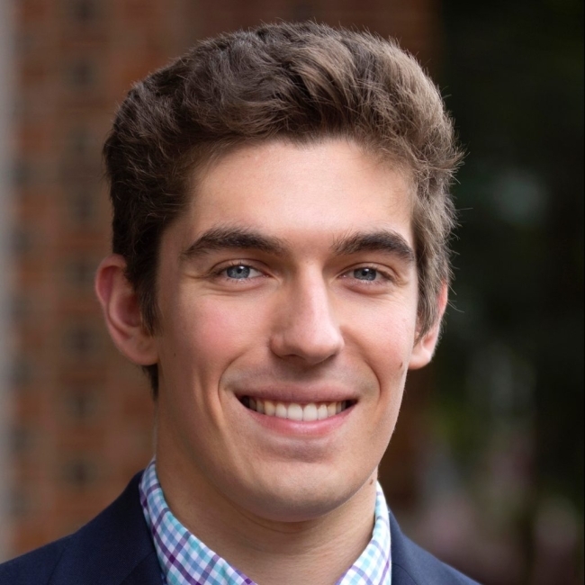 a young white man wearing a suit and tie smiling outside