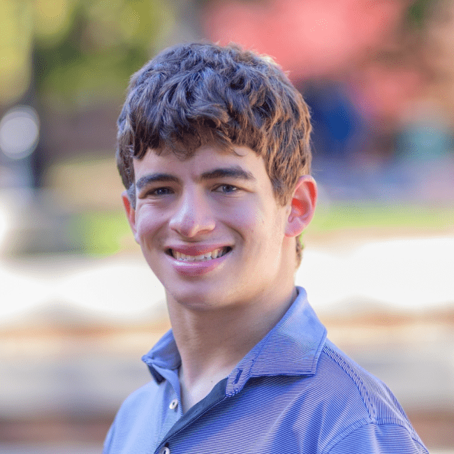 a young white man with brown hair wearing a purple collared shirt