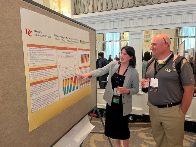 a young woman presents a poster to an older man