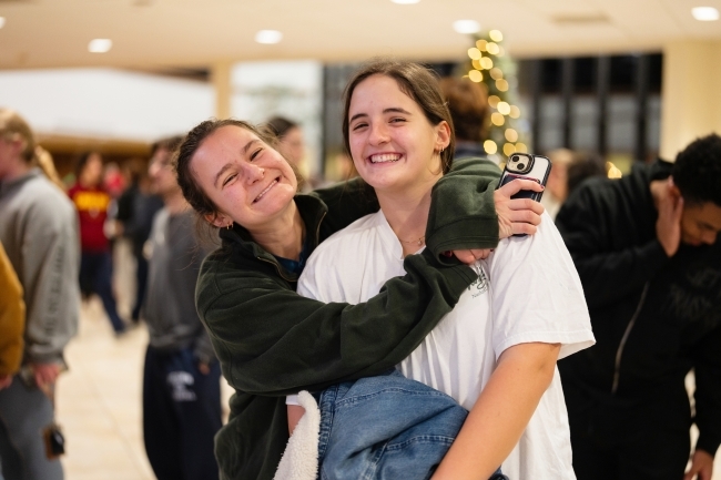 two young women smile and hug each other in a dining hall