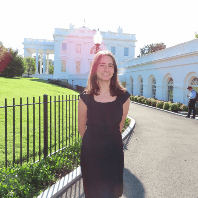 a young white woman wearing a black dress standing in front of the White House