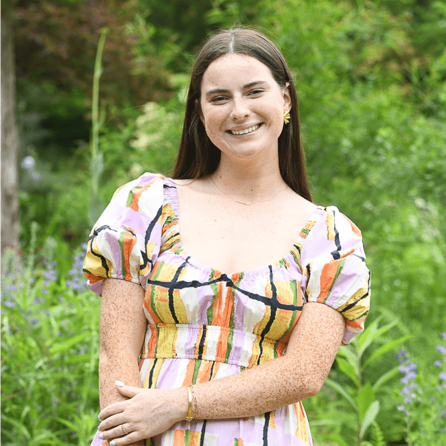 a young woman with long dark hair wearing a colorful dress in a green field