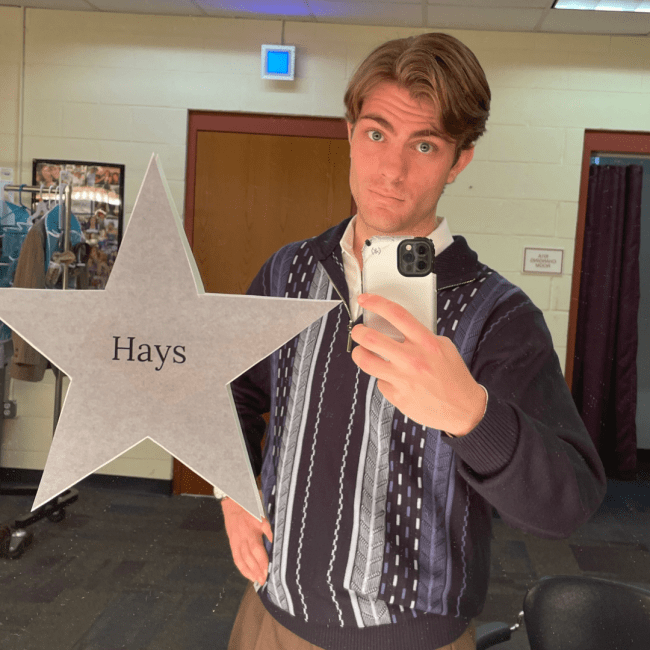 a young man with short hair wearing a sweater and taking a selfie in a mirror