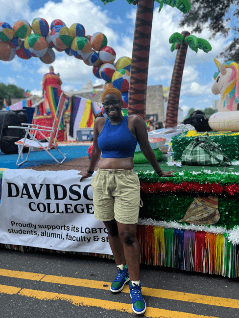 a young Black woman poses in front of a pride day float