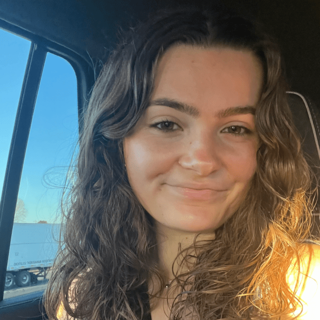 a young woman with curly brown hair smiling in a car