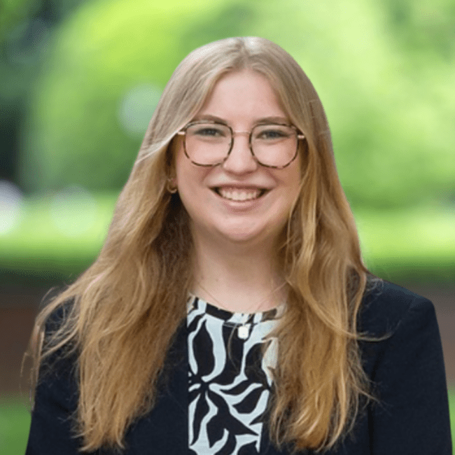 a young woman with blonde hair wearing a blazer and glasses
