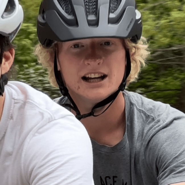 a young man with blonde hair wearing a bike helmet and grey tshirt