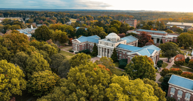 an aerial view of a college campus with brick buildings, green trees and a lake in the distance