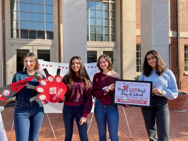 a group of four young women smile and hold a sign that reads "happy last first day of school"