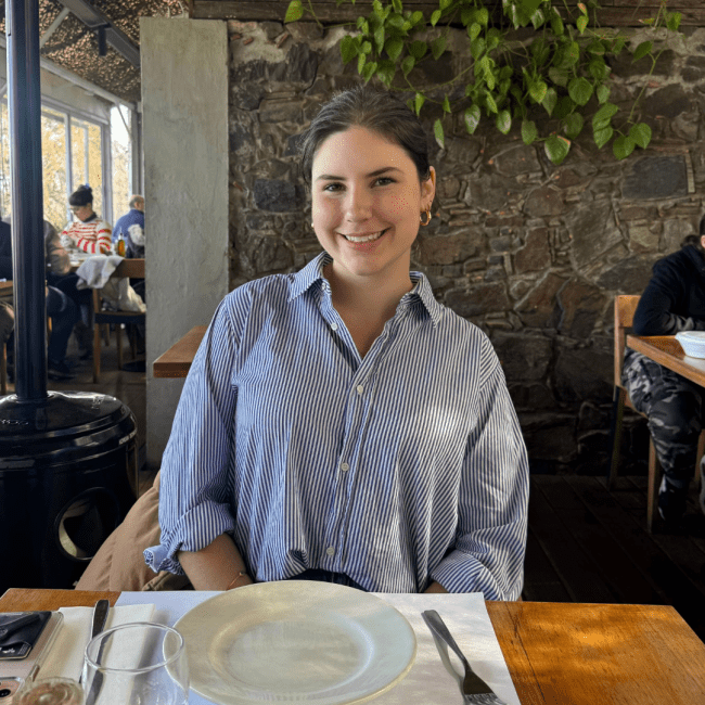 a young woman wearing a blue collared shirt sitting at a table 