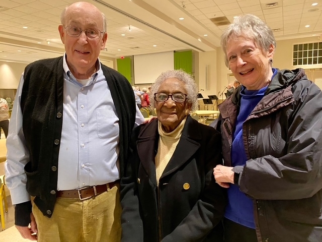 An elderly white man, black woman, and white woman stand in a row