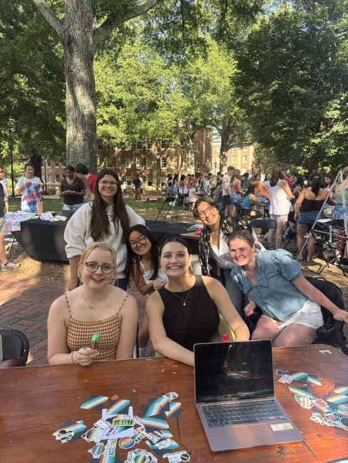 a group of students sit at a table outside smiling with a laptop