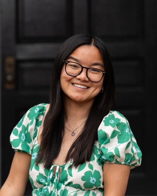 a young woman with black hair and glasses smiling wearing a green and white floral dress