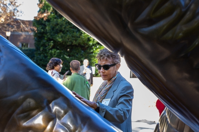 Attendee wearing sunglasses touches the sculpture of the hands