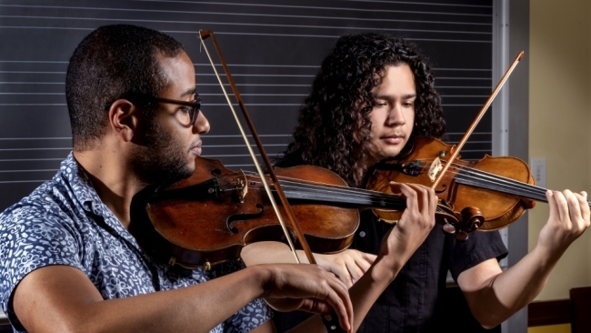 Two men play the violin next to each other