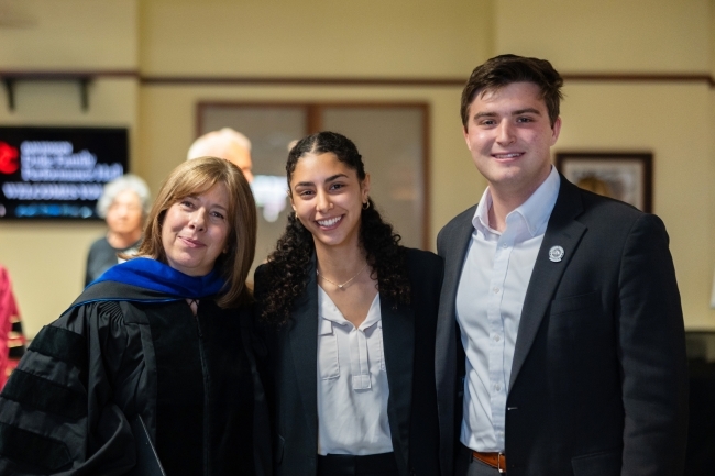 two students with a faculty member smiling and wearing business clothes