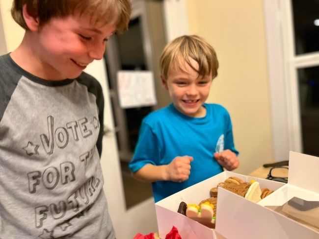 Two boys, one younger and one older, excitedly open a box of cookies