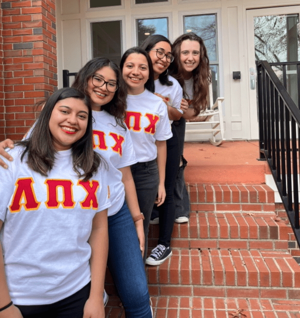 Five young college students wearing matching grey shirts with red greek lettering across the chest