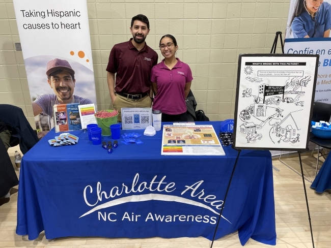 Two people stand behind a table with a blue tablecloth that says "Charlotte Area NC Air Awareness"