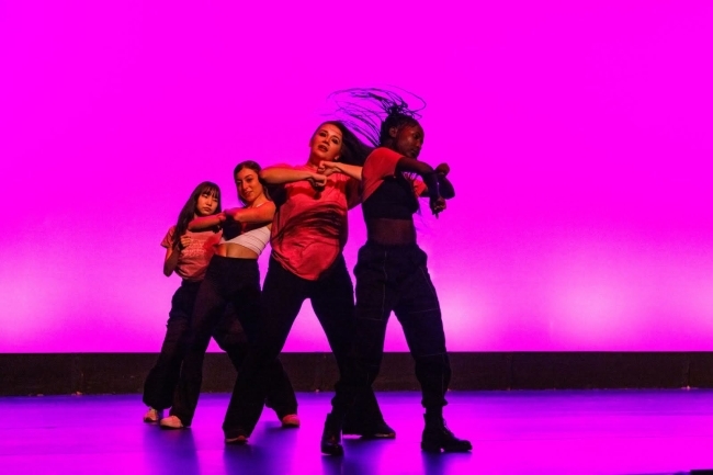 a group of your women dance onstage in front of a magenta backdrop