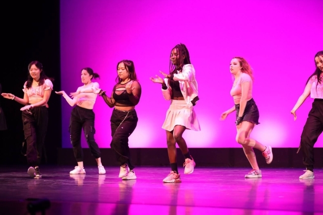 a group of young women dance on stage in front of a pink backdrop