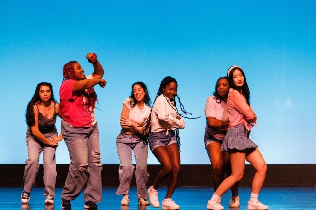 a group of young women dance onstage in front of a light blue backdrop