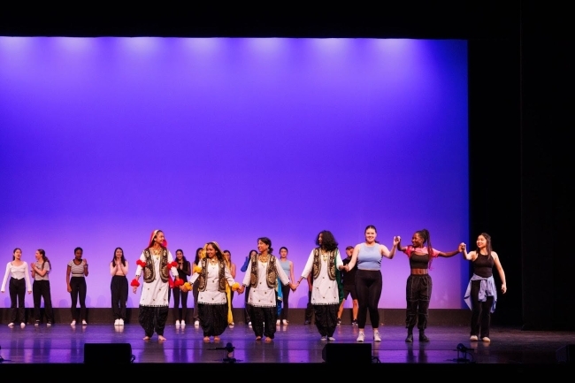 a group of students dance on stage in front of a blue backdrop