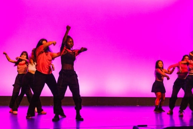 a group of young women dance onstage in front of a magenta backdrop