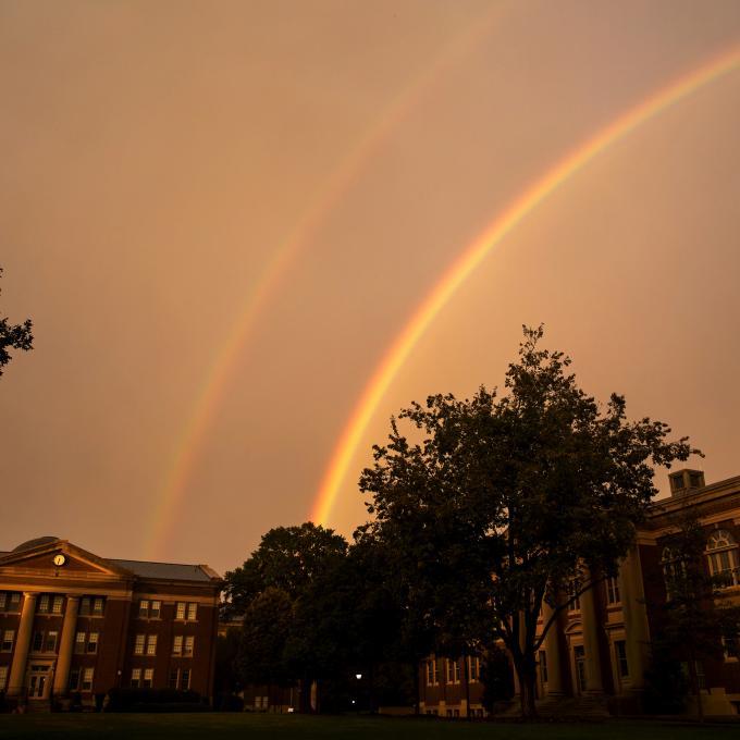 Sky rainbow over college buildings and trees 