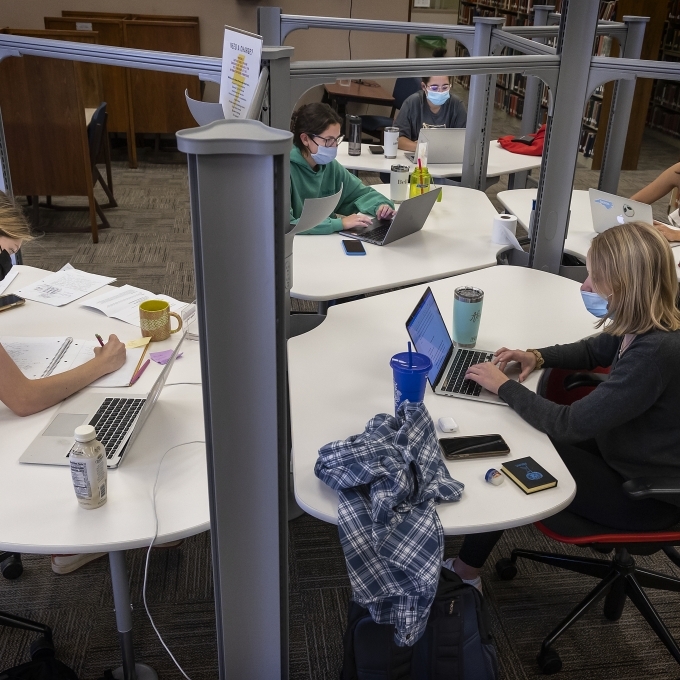 Group of students studying at pod of desks in library for final exams