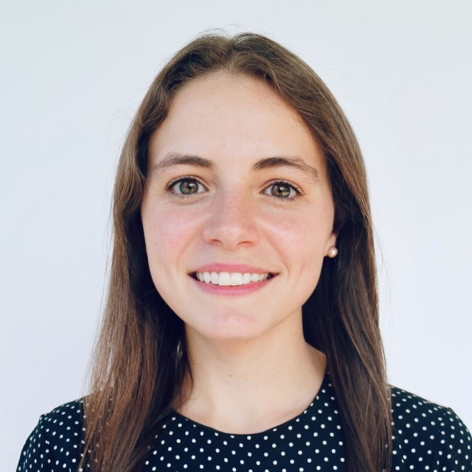 A white woman smiling wearing a polka dot shirt with brown hair