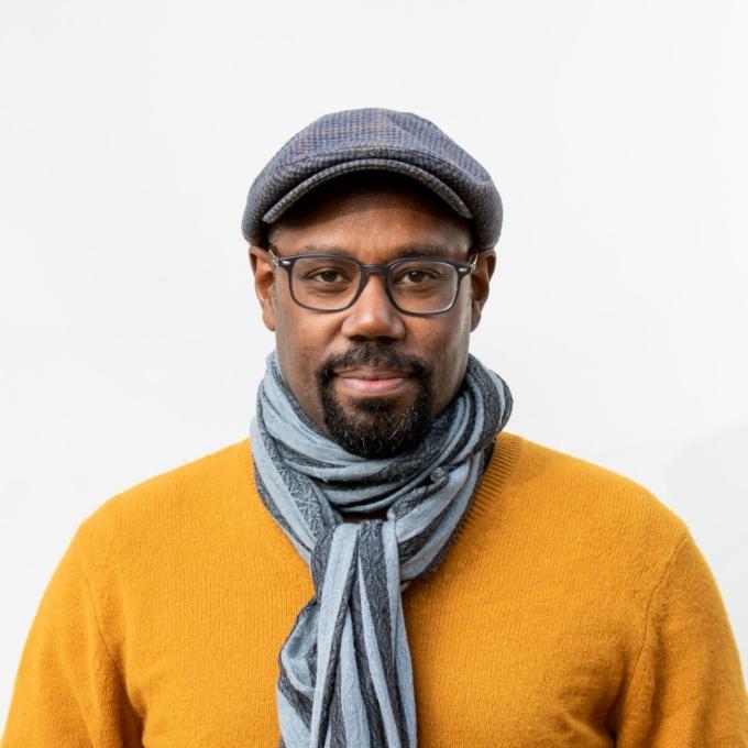 a young Black man wearing a yellow sweater, scarf, hat and glasses