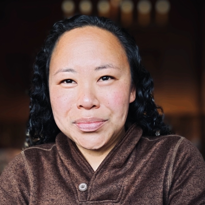 a young woman with black hair wearing a brown sweatshirt and smiling