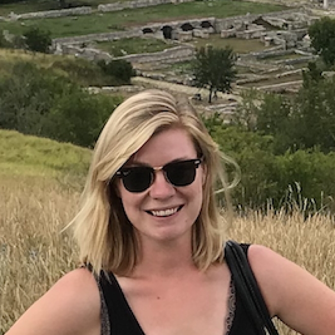 a young white woman with blonde hair wearing sunglasses standing in front of ancient ruins