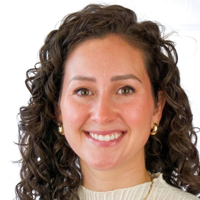 a young white woman with brown hair wearing a white top and gold necklace