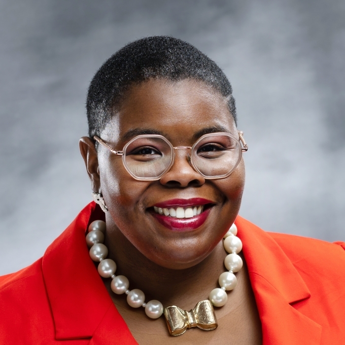 a Black woman wearing glasses and a bright orange blazer