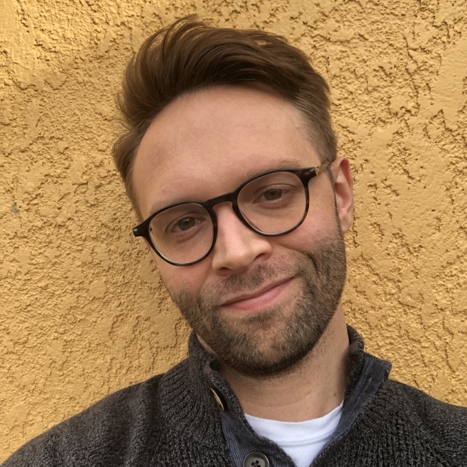 a young man wearing glasses and a grey sweater with short brown hair
