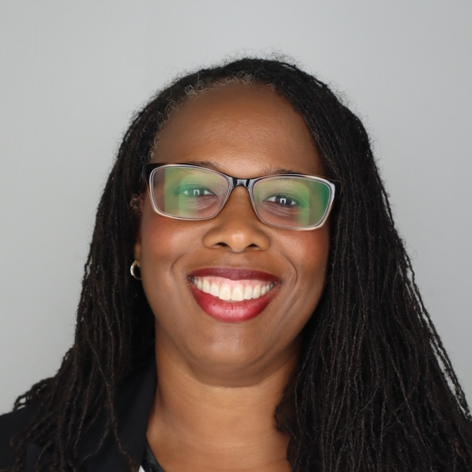 a middle aged Black woman with long dark hair wearing glasses and red lipstick on a grey background