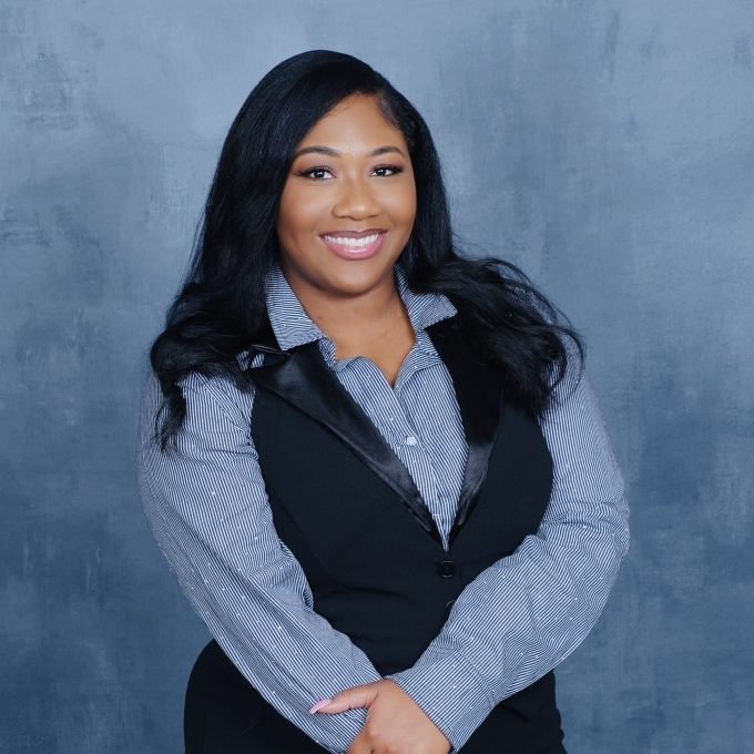 a young Black woman wearing a collared dress shirt and vest in front of a blue background