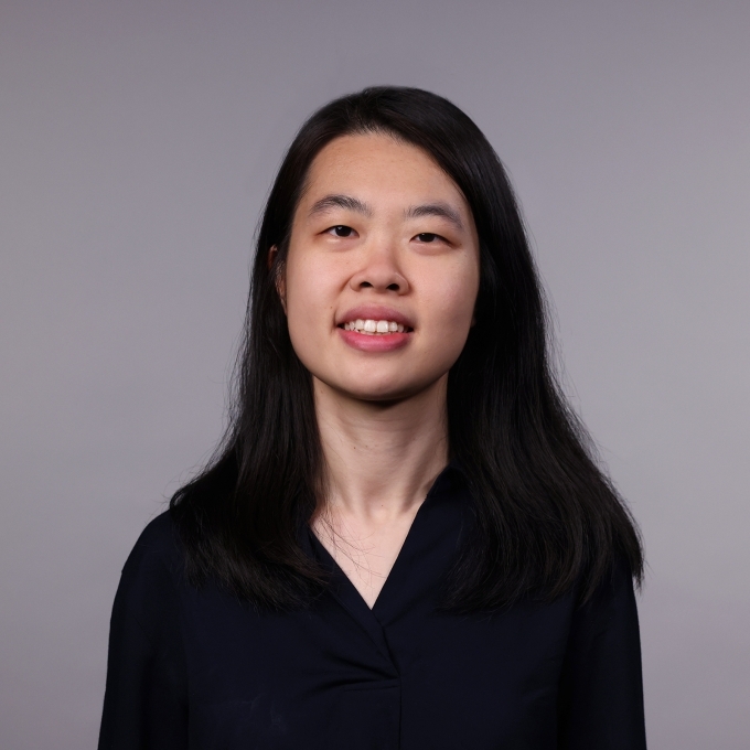 a woman with long black hair wearing a black blouse smiling on a grey background