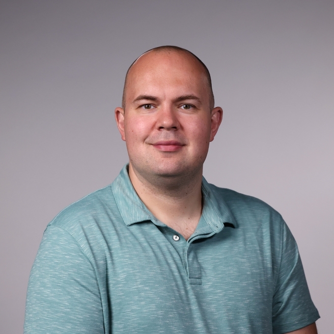 a man wearing an aqua polo smiling on a grey background