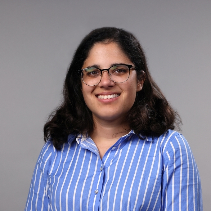 a woman with dark hair wearing glasses and blue striped collared shirt on a grey background